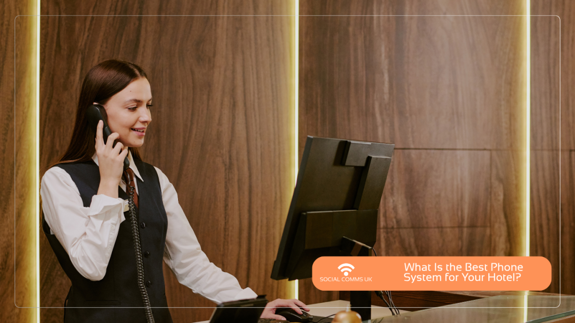 A woman in hotel reception uniform speaking on a telephone in front of a monitor, beside a wood-paneled wall. Social Comms UK asks, "What is the Best Phone System for Your Hotel?".