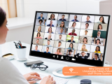 A woman sitting at a desk looking at a computer screen showing a large video conference call with dozens of participants. In the bottom right, an orange banner features the Social Comms UK logo and the text "Why Schools and Universities Need a Modern VoIP Phone System."